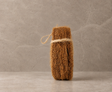 Natural handmade coir scrubber resting on a stone surface